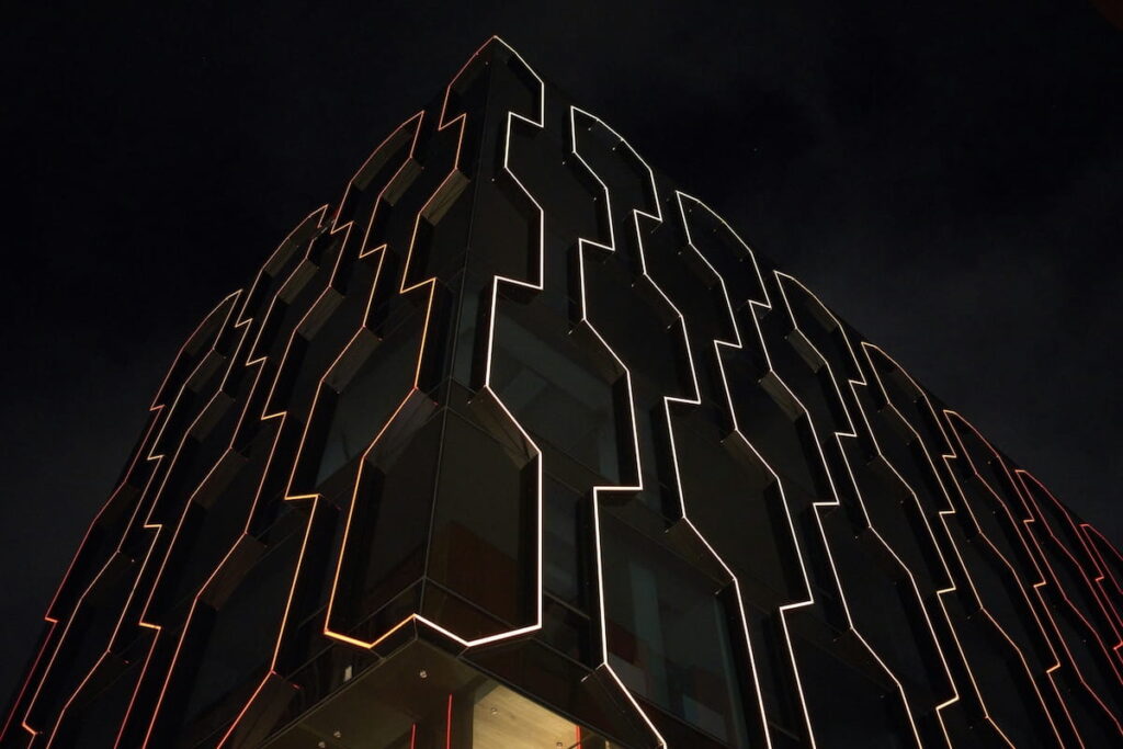 Modern office building in Tallinn with a dark glass facade and orange illuminated geometric patterns against the night sky.